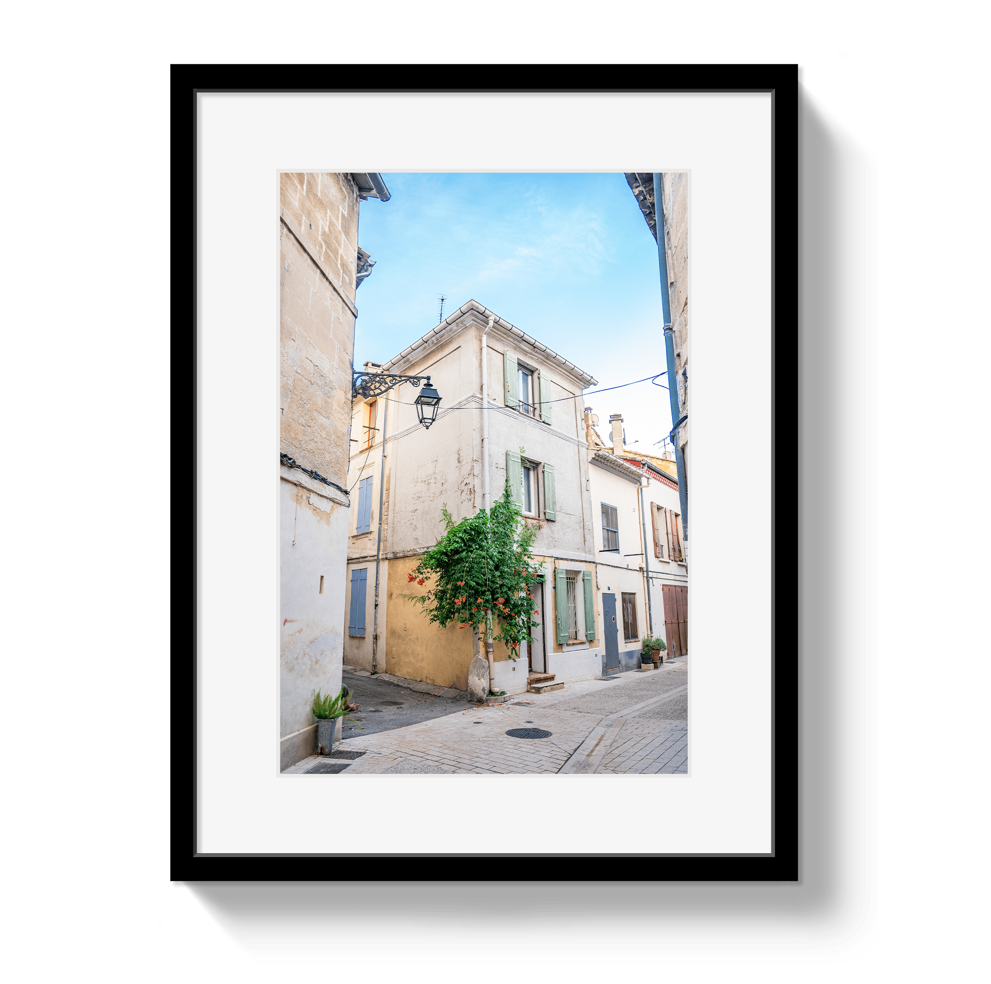 Framed photograph of a narrow street with buildings and a tree.