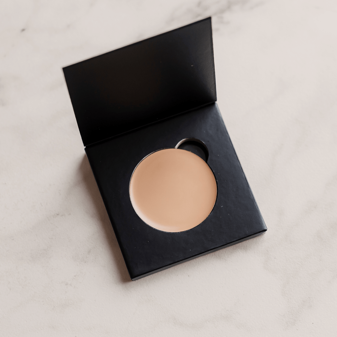 Compact powder in a black case on a light marble background