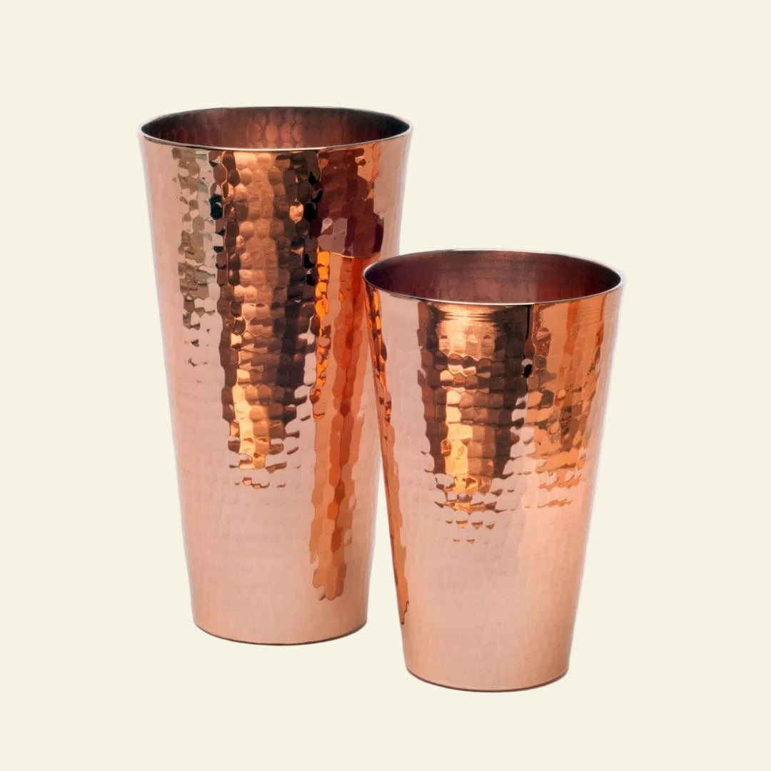 Two copper tumblers with a hammered finish on a white background