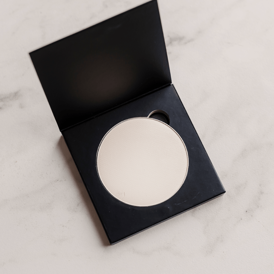 Round compact mirror in a black case on a light marble surface