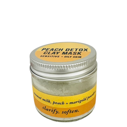 A small clear glass jar of peach detox clay mask with a silver metal lid and a yellow label, shown on a plain white background.