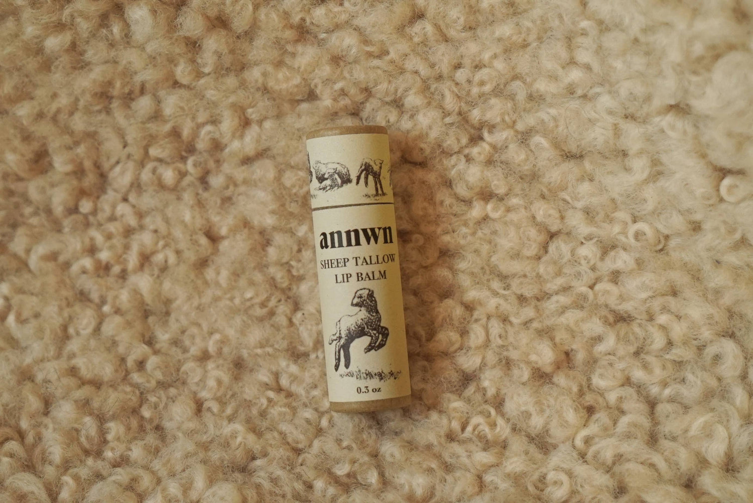 Roll of Annwn sheep tail wool lip balm on a textured beige surface