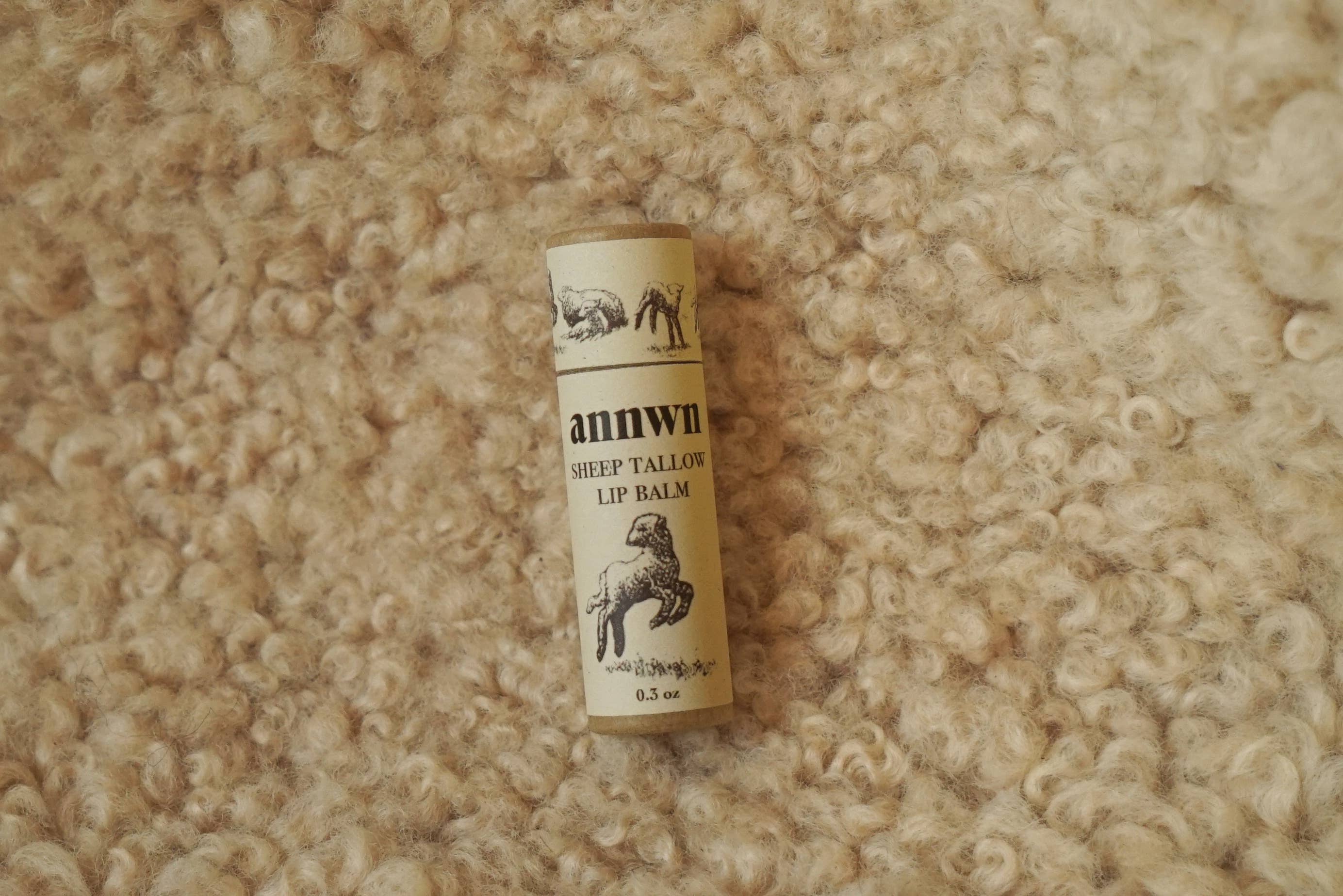 Roll of Annwn sheep tail wool lip balm on a textured beige surface