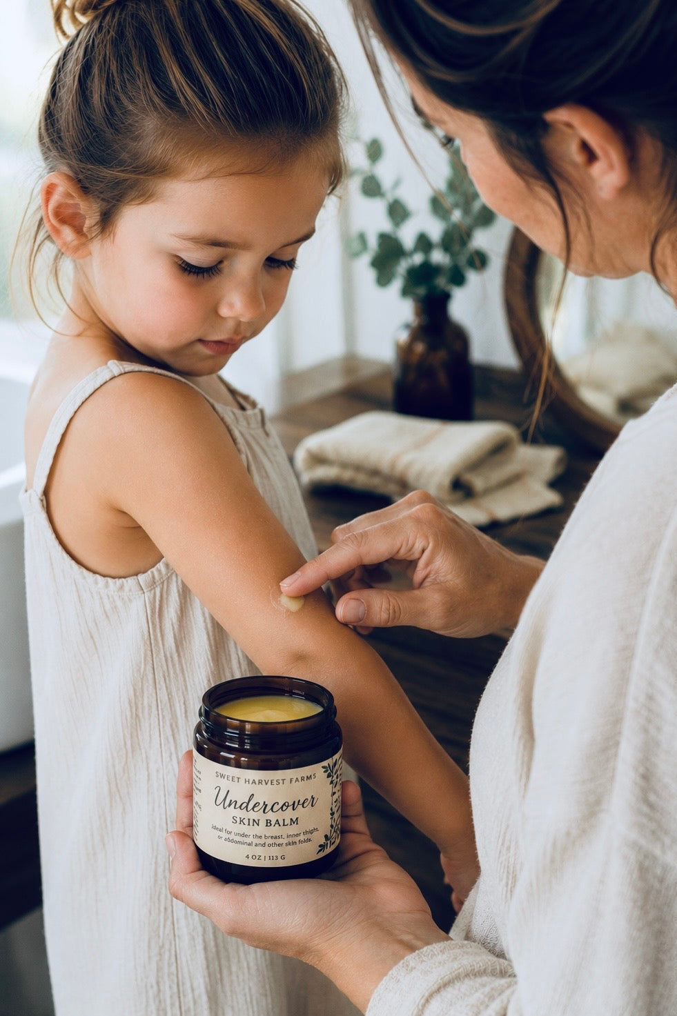 A woman applies cream balm from a dark amber jar labeled &