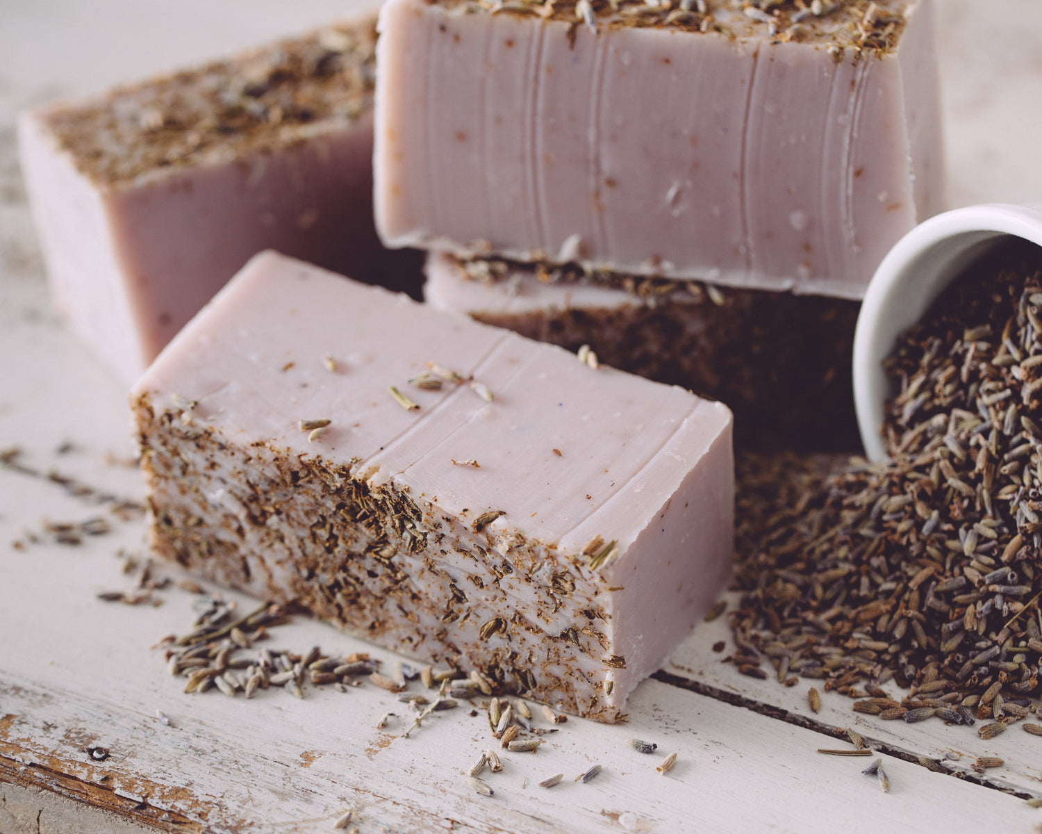 Pink soap bars with specks on a wooden surface, surrounded by lavender flowers.
