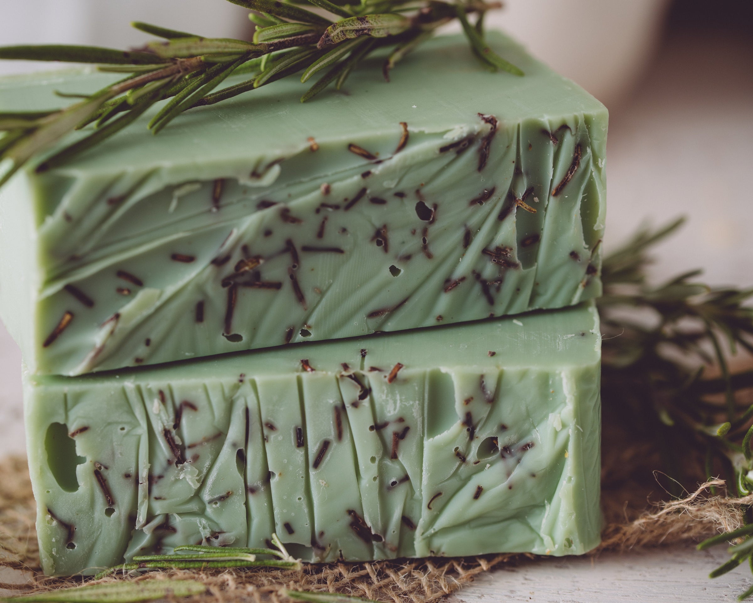 Green soap bar with specks on a wooden surface with rosemary leaves.
