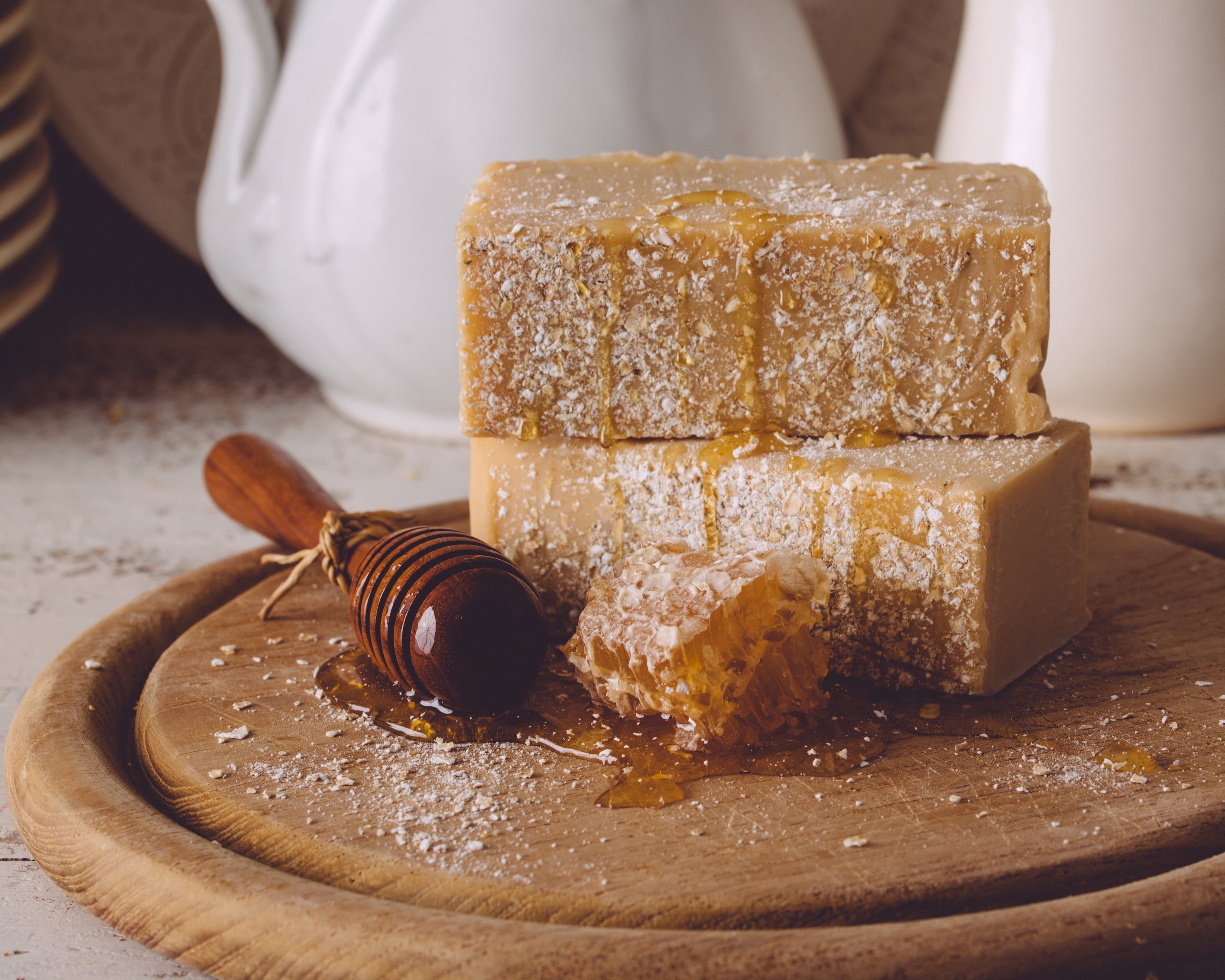 Three pieces of honeycomb with honey on a wooden board, with a white teapot in the background.