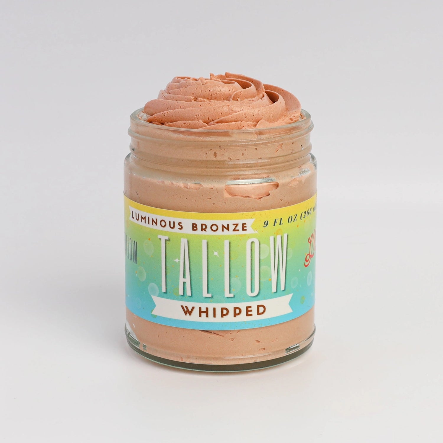 An open glass jar of Tallow Whipped body butter, showing the light brown whipped product inside, topped with a swirl of the same product. The jar has a colorful label with &