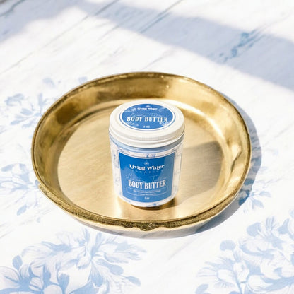 Jar of body butter on a gold tray with a blue label against a light floral background