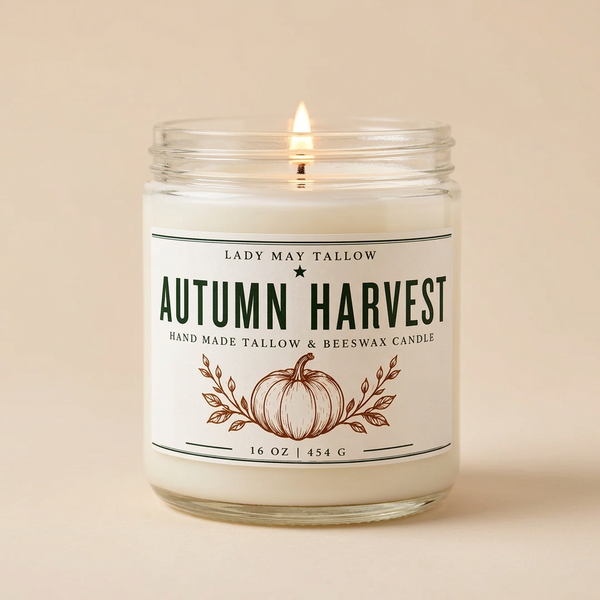 A lit 'Autumn Harvest' scented candle by Lady May Tallow in a clear glass jar with a white label featuring a brown pumpkin illustration, set against a solid beige background.