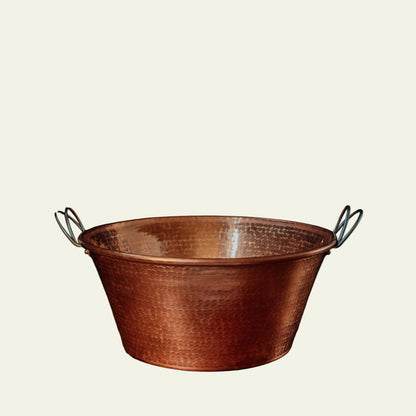 Copper basin with handles on a wooden surface against a dark background