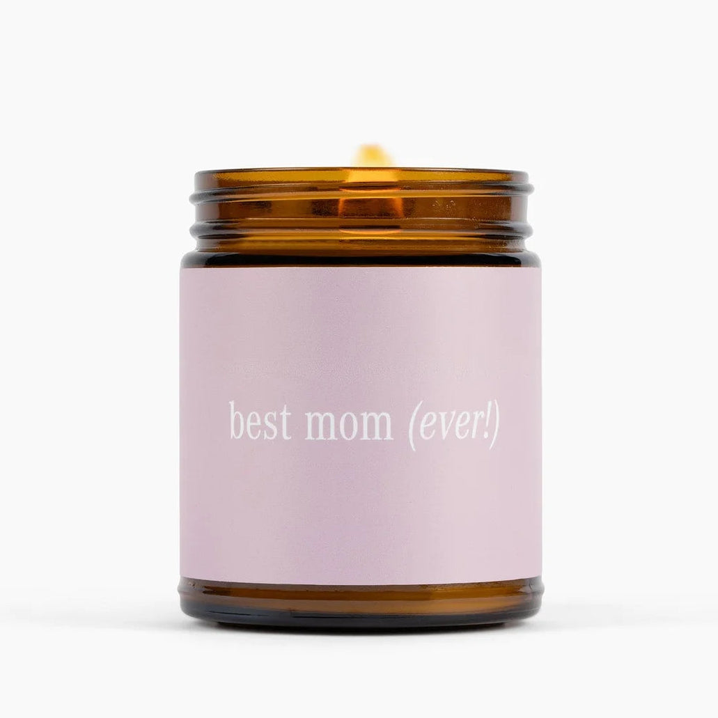 An amber glass jar candle with a lit wick and a light pink label that reads &