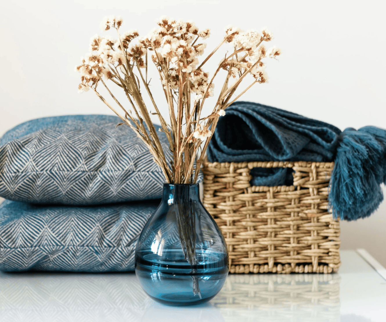 Blue vase with dried flowers on a surface with towels and a basket in the background