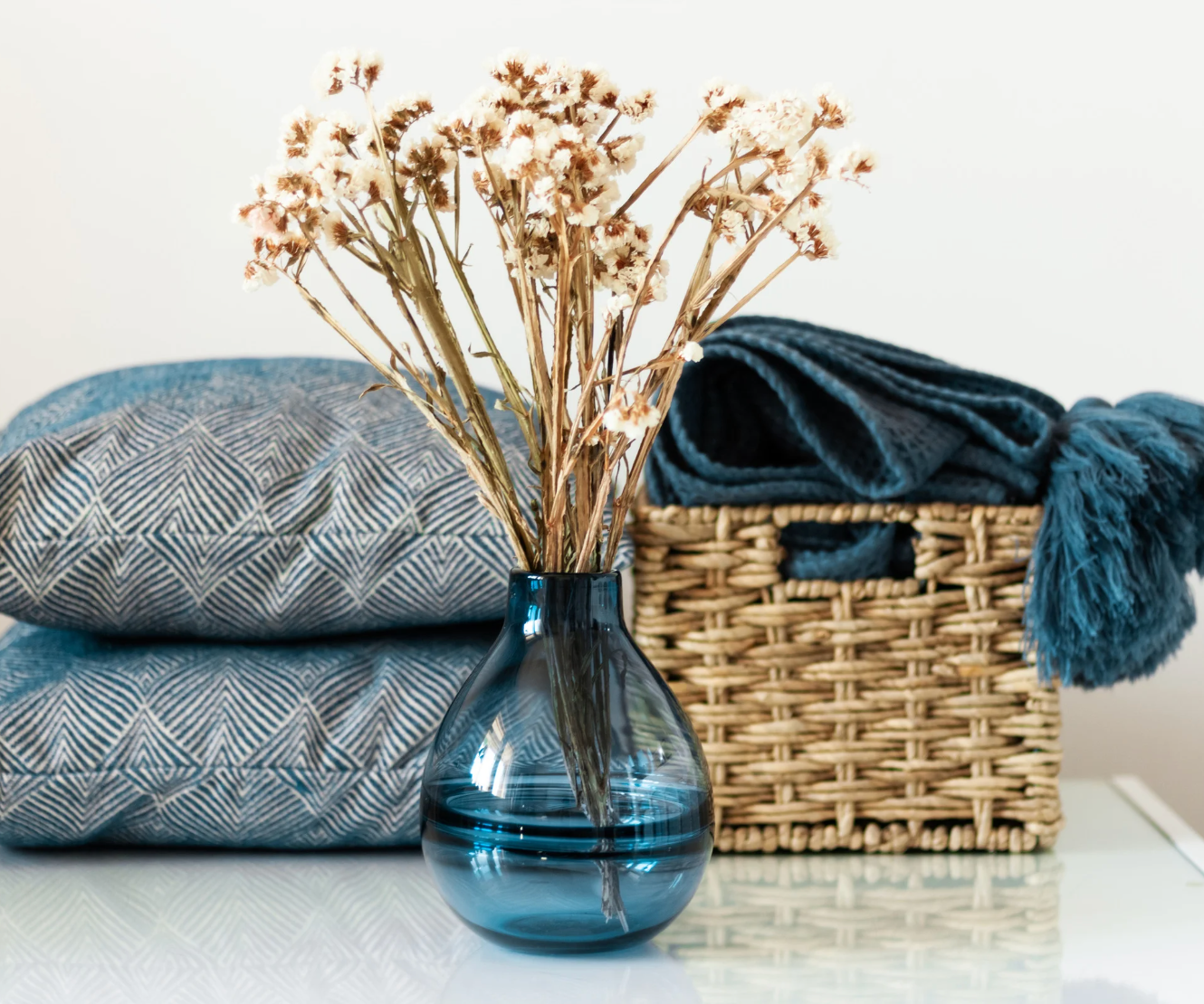 Blue vase with dried flowers on a surface with towels and a basket in the background