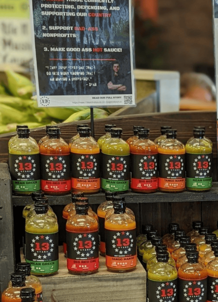 Bottles of a hot sauce brand with a sign in the background