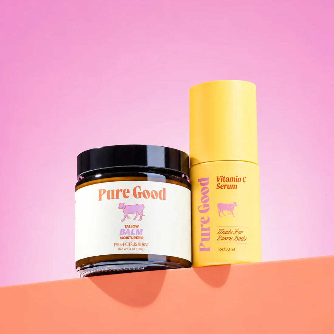 Pure Good skincare products, including a jar of Salve Balm and a bottle of Vitamin C Serum, displayed on a peach-colored surface against a pink background.
