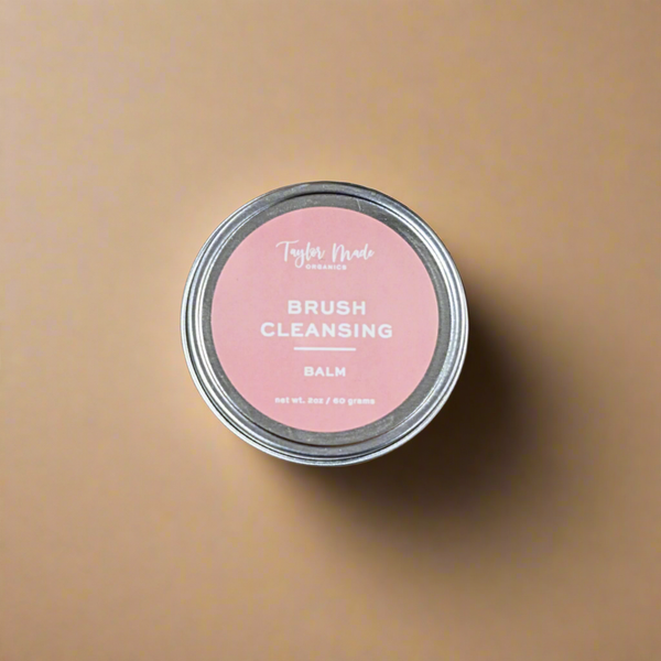 Tin of brush cleansing balm with pink label on a beige background