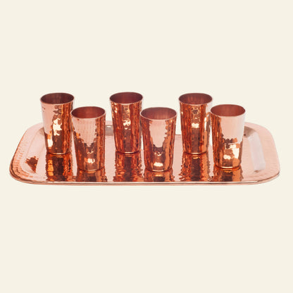 Set of six copper shot glasses on a matching tray with a white background