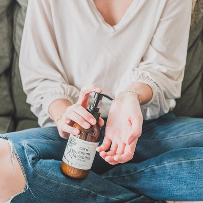 Person applying a brown bottle of lotion to their hand on a couch.