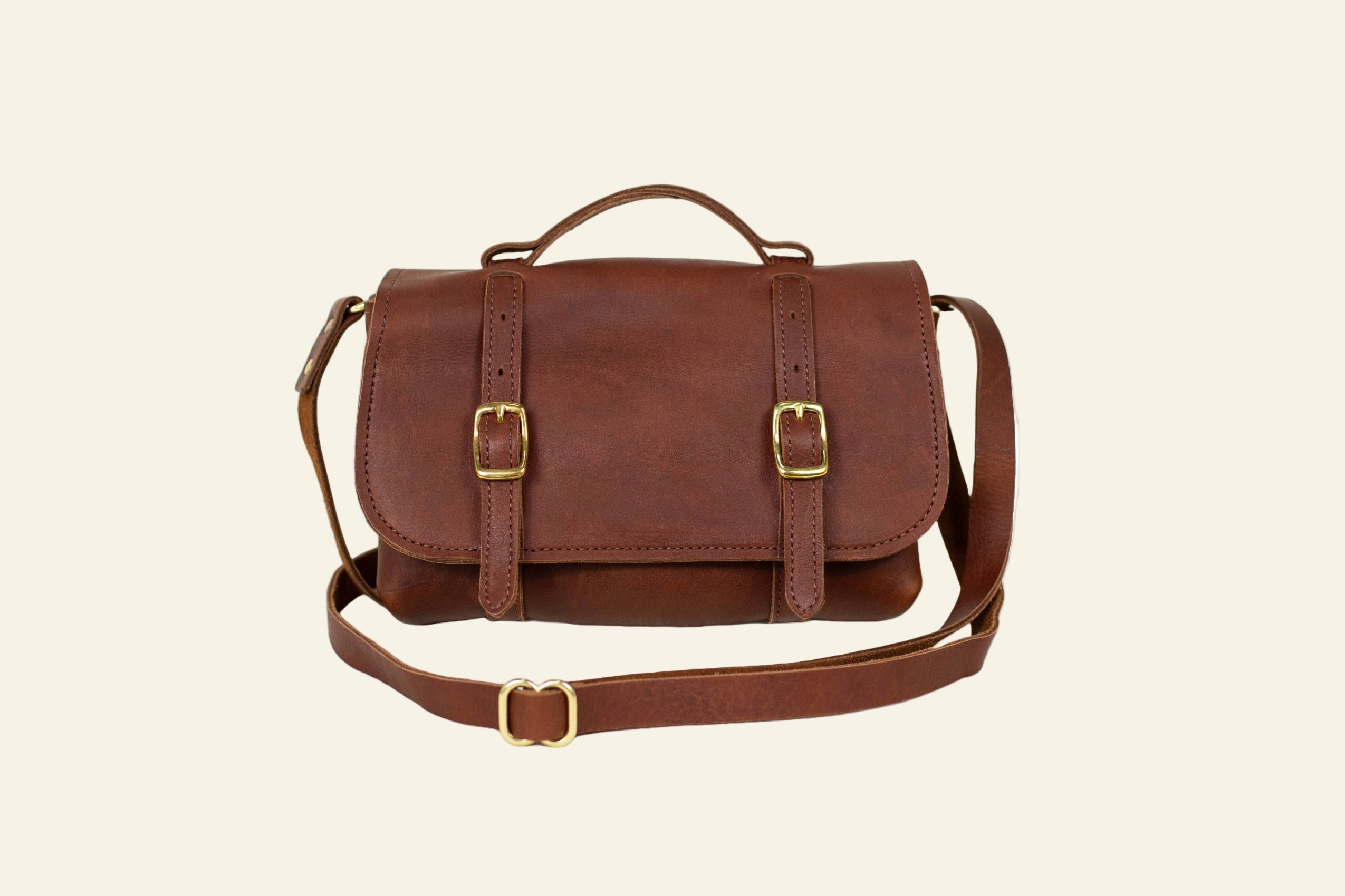 Brown leather satchel bag with gold buckles on a white background