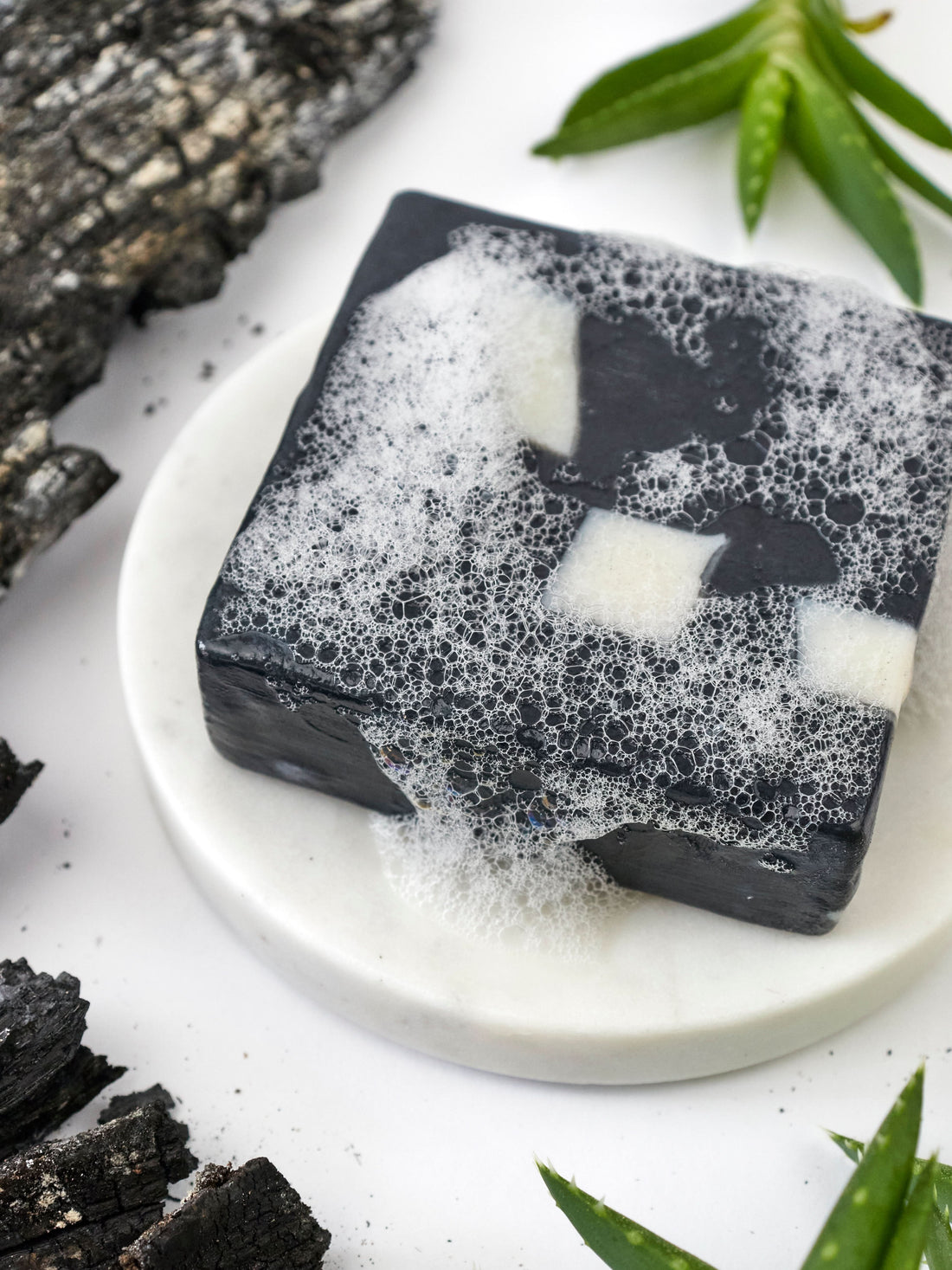 Black and white soap bars on a white plate with green leaves in the background