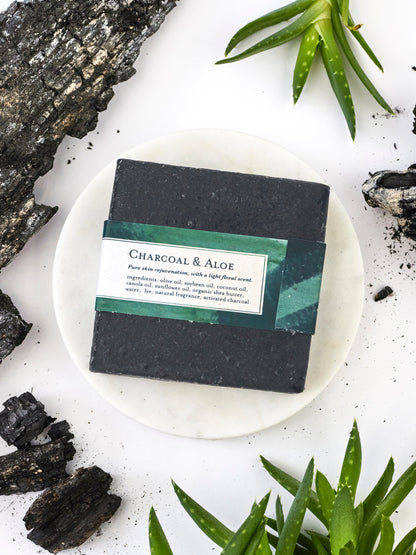 Bar of charcoal and aloe soap on a white plate with natural elements around
