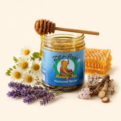 A jar of ZerBear Organic Honey Tea Nocturnal Nectar with a wooden honey dipper resting on top, surrounded by chamomile flowers, lavender, roots, and a piece of honeycomb on a warm cream background.
