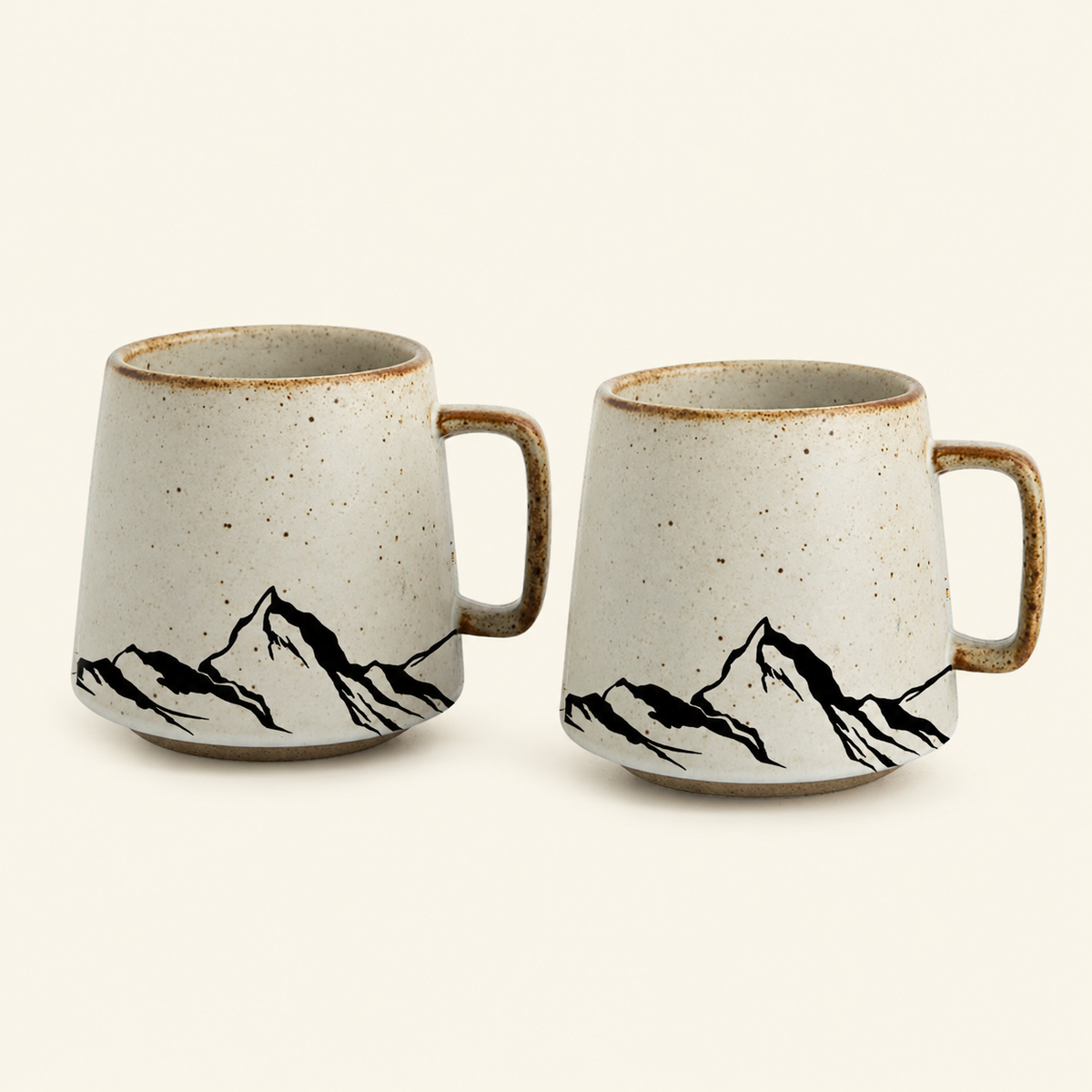 Two ceramic mugs with a speckled off-white glaze, brown rim, and black mountain line art, shown on a plain light beige background.