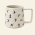 A speckled off-white ceramic mug with a handle, decorated with a repeating pattern of small skiers and snowboarders in various colorful outfits, set against a solid cream background.