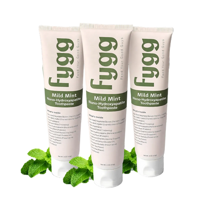 Three tubes of Fygg Mild Mint Nano-Hydroxyapatite Toothpaste arranged in a fan shape with mint leaves at the base, set against a black background with a light mint splash graphic.
