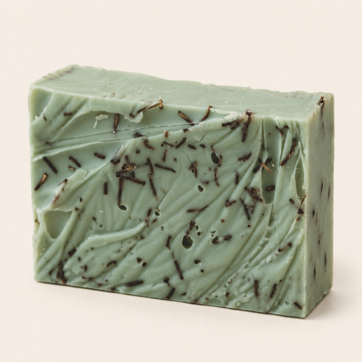 A rectangular bar of handmade soap in a pale mint green color, decorated with dark brown dried flower petals, shown on a plain light beige background.