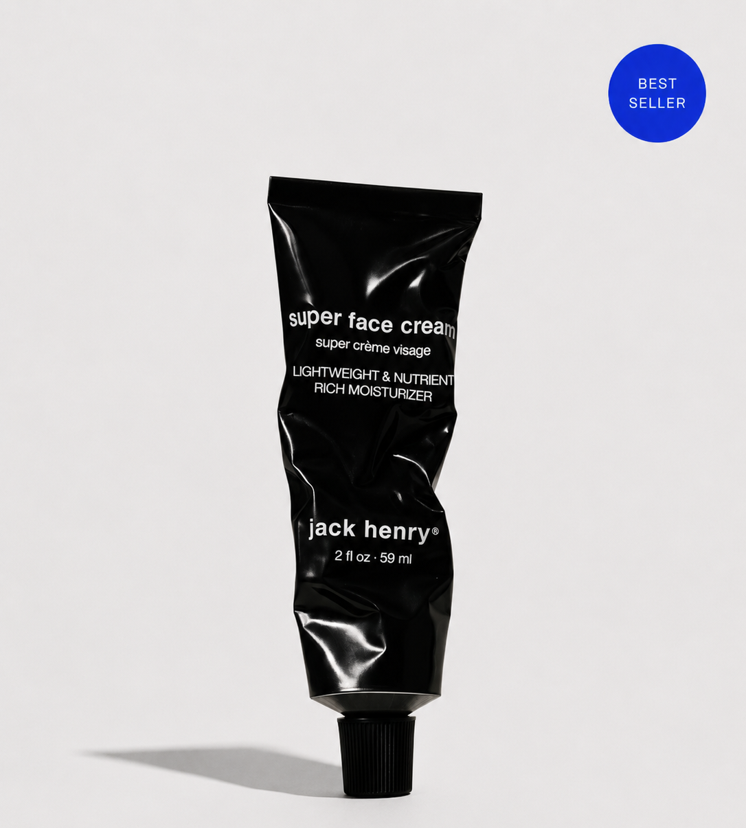 A black squeeze tube of Jack Henry Super Face Cream with white text, shown on a light gray background with a blue &
