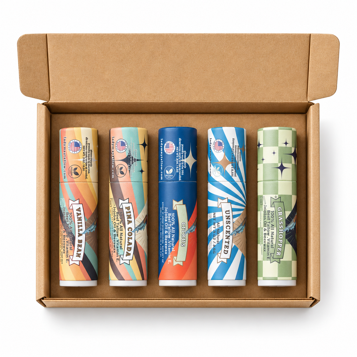 Five lip balm tubes in assorted flavors arranged inside an open brown cardboard box on a white background. The tubes feature colorful retro-style labels with text including Vanilla Bean, Pink Collar, Cotton Candy, Upside Down, and Classic Chocolate.