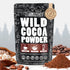A stand-up pouch of Wild Cocoa Powder by Wild Foods Product, shown on a light gray background with cocoa beans and cocoa powder piles in the foreground. The package is black with white text and illustrated graphics, plus brown label panels near the bottom.