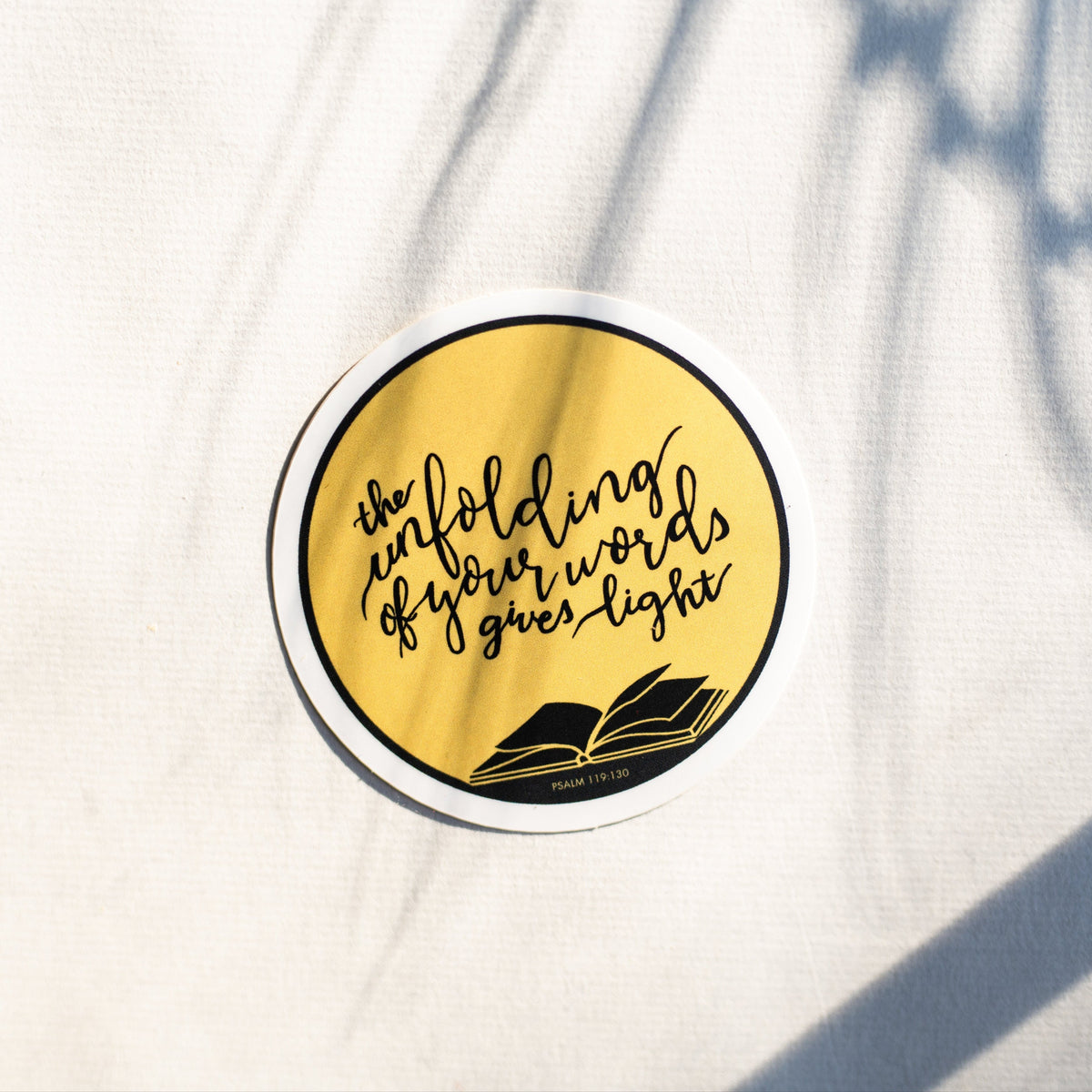 A round sticker with a yellow background, black border, and black text reading &