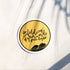 A round sticker with a yellow background, black border, and black text reading &