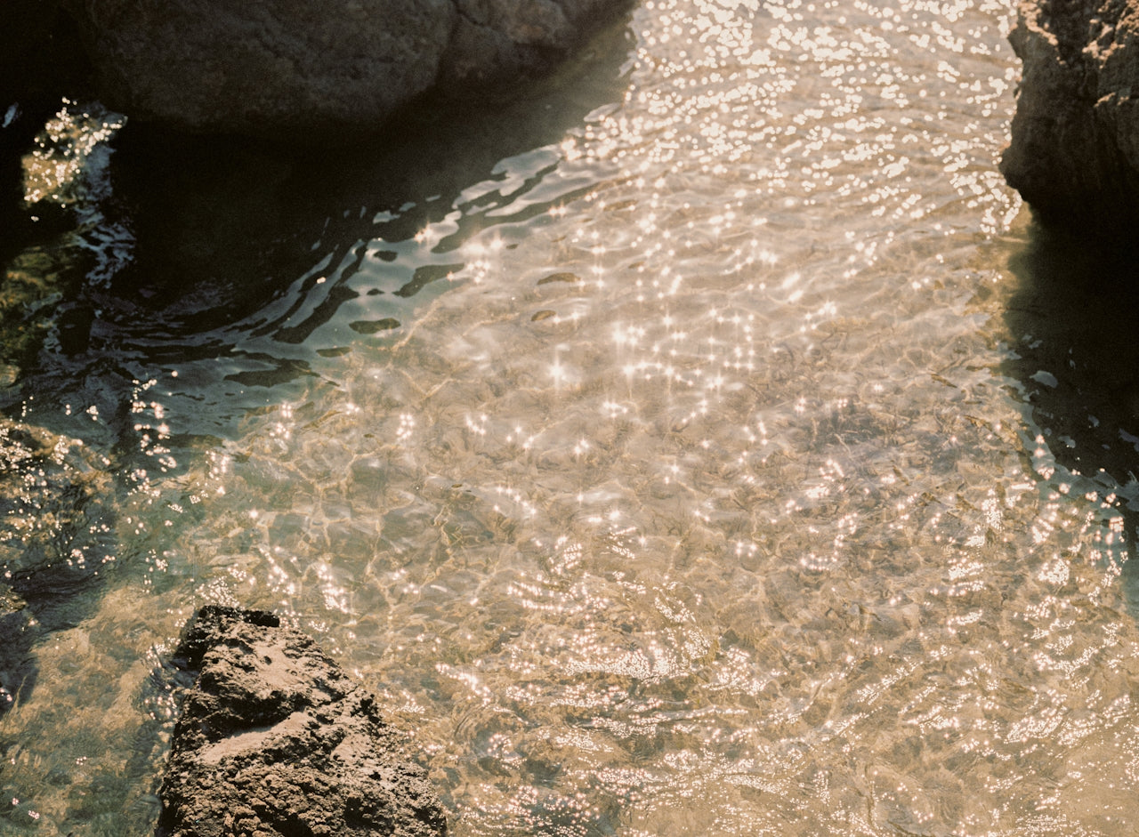 Clear water with sunlight reflecting off the surface, surrounded by rocks.