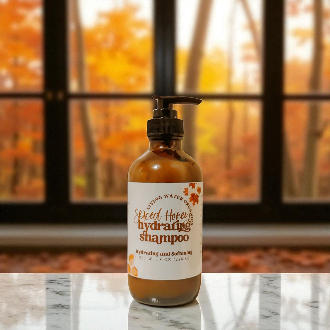 Bottle of Spiced Honey Hydrating Shampoo on a marble surface with autumn foliage in the background