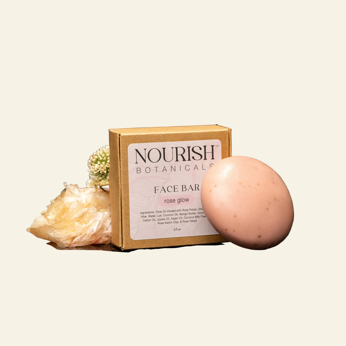A bar of Nourish Botanicals Rose Glow face bar soap is displayed next to its cardboard packaging box on a reflective black surface, styled with dried sea plants against a dark textured background.
