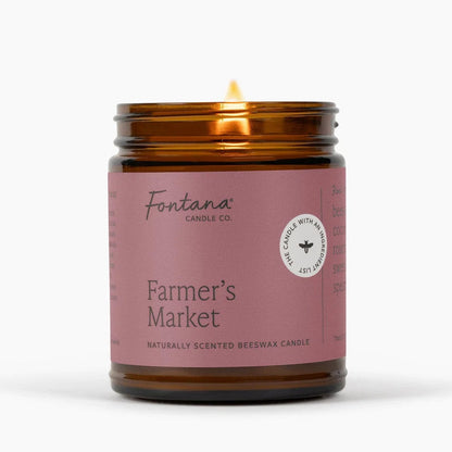 A lit amber glass jar candle with a dusty pink label reading &