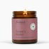 A lit amber glass jar candle with a dusty pink label reading &