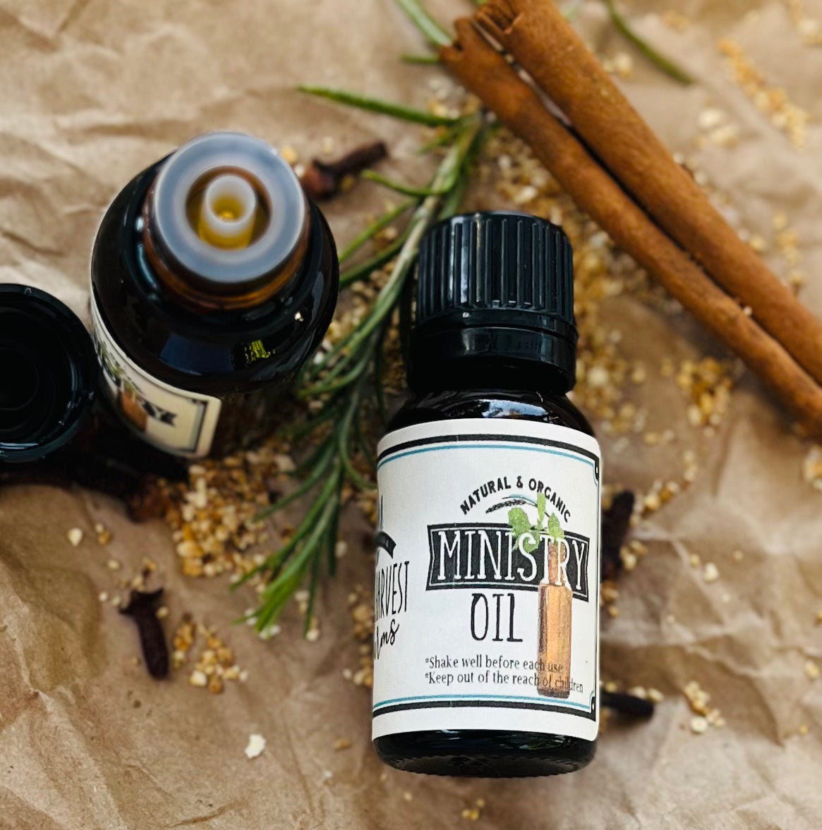 Bottle of Ministry Oil with cinnamon sticks and rosemary on a textured surface