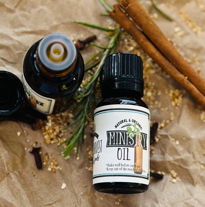 Bottle of Ministry Oil with cinnamon sticks and rosemary on a textured surface