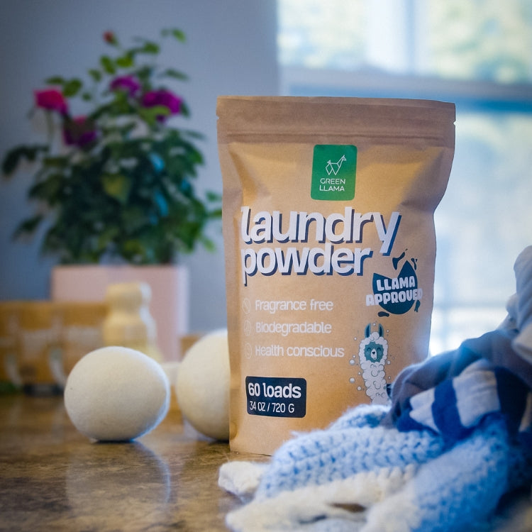 Package of laundry powder with detergent balls on a wooden surface, plant and window in the background