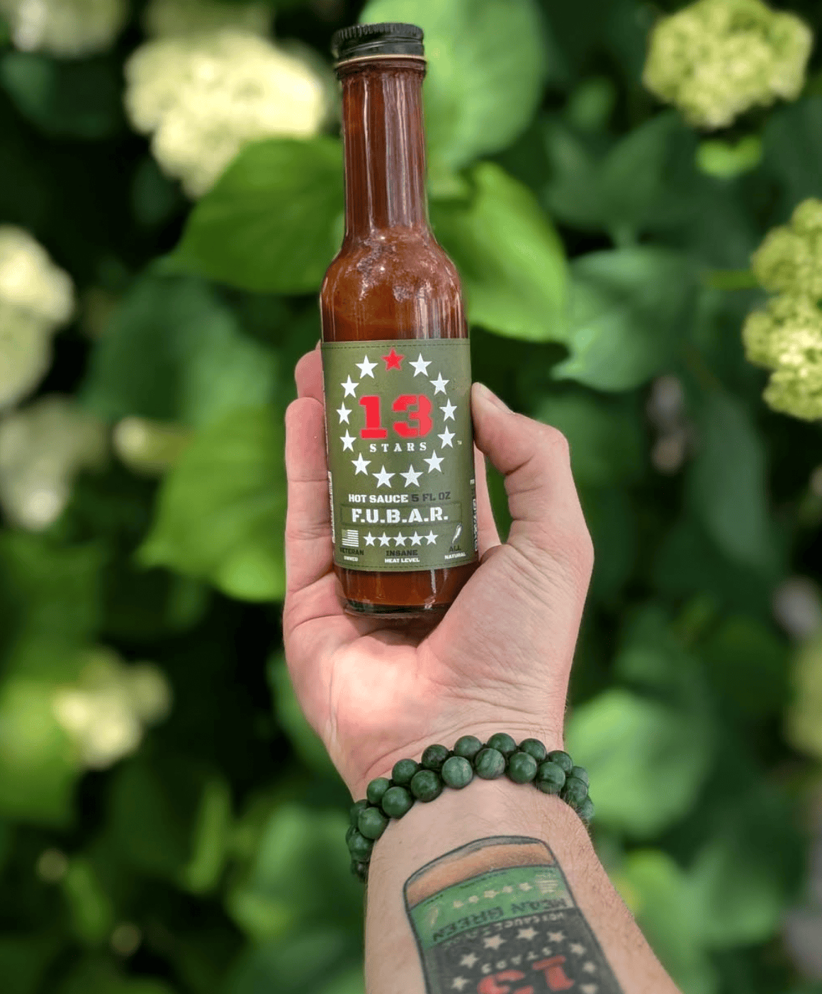 Hand holding a bottle of FUBAR hot sauce with a green label against a blurred natural background