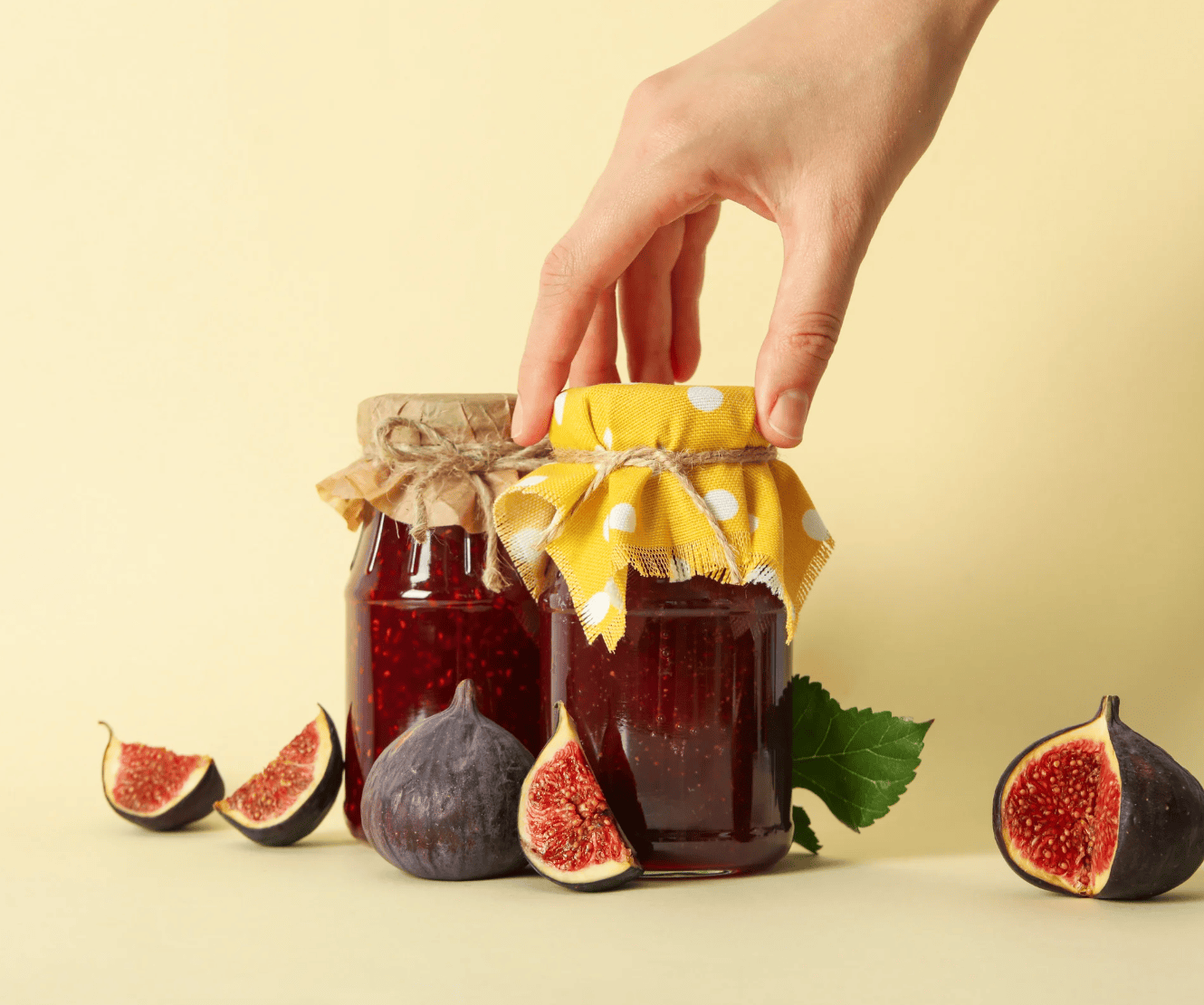 Hand reaching for a jar of jam with figs on a light yellow background