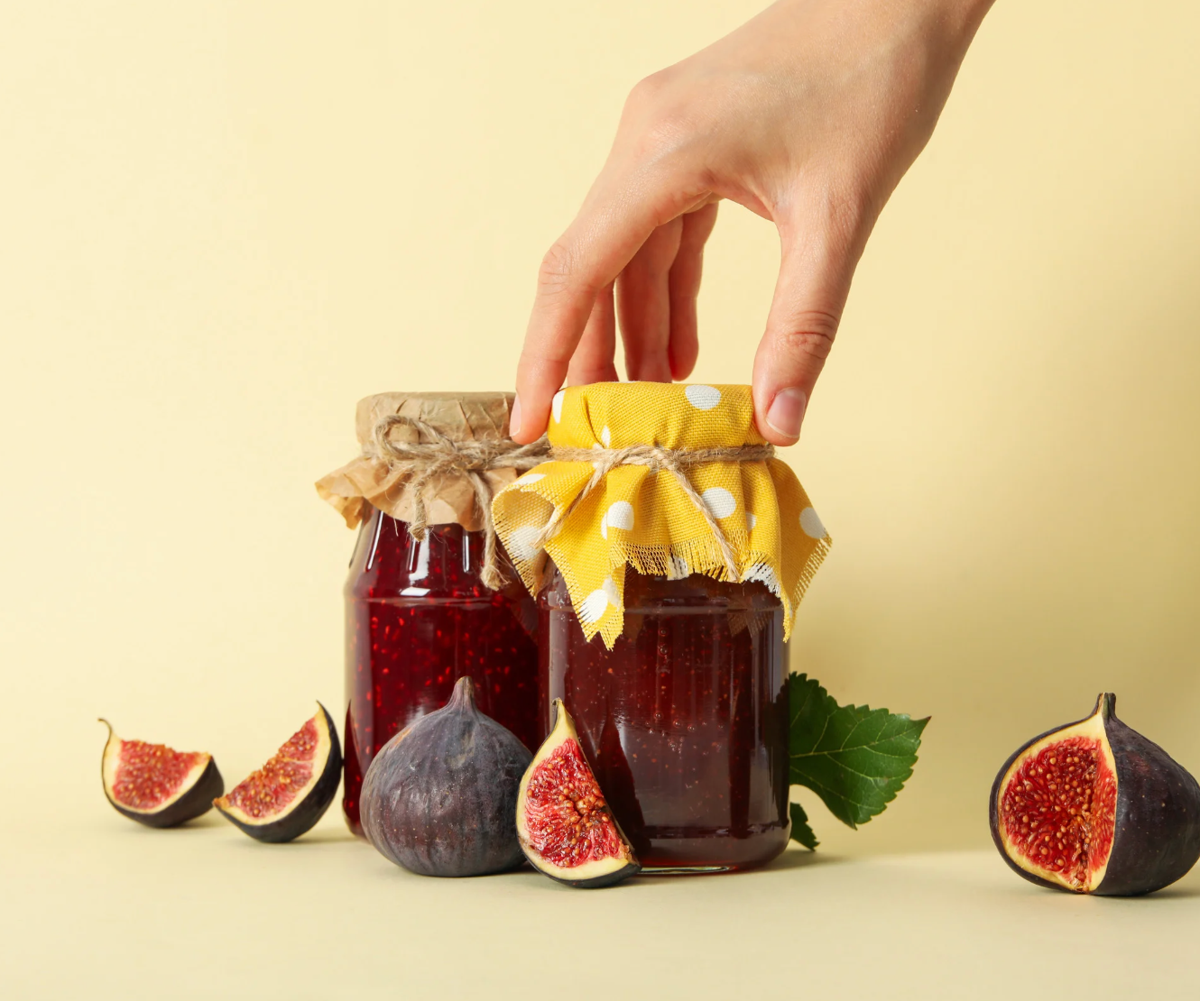 Hand reaching for a jar of jam with figs on a light yellow background