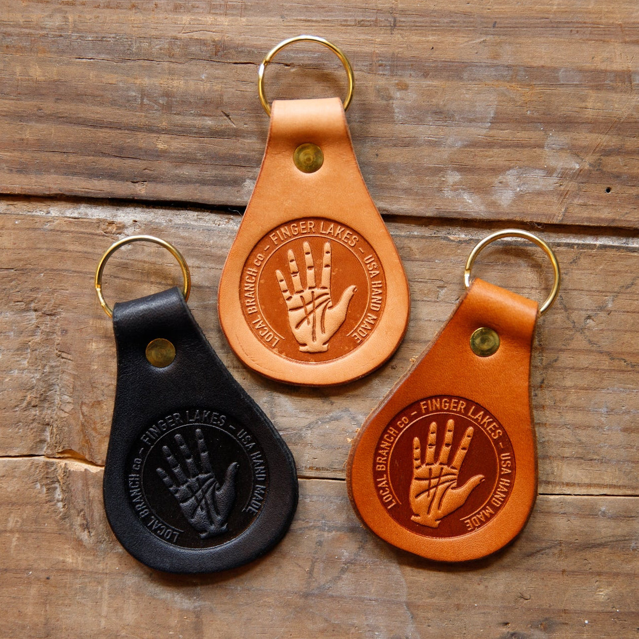 Three leather keychains with hand design embossing on a wooden surface