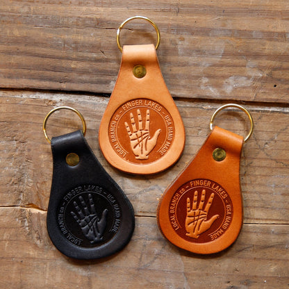 Three leather keychains with hand design embossing on a wooden surface