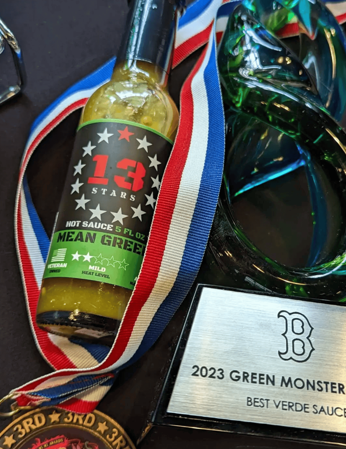 Hot sauce bottle with decorative ribbon and award plaque on a dark surface